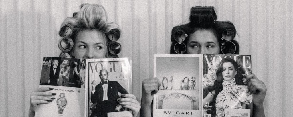 Two women in hair rollers holding fashion magazines